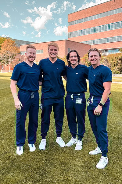 Four male dental students in navy scrubs