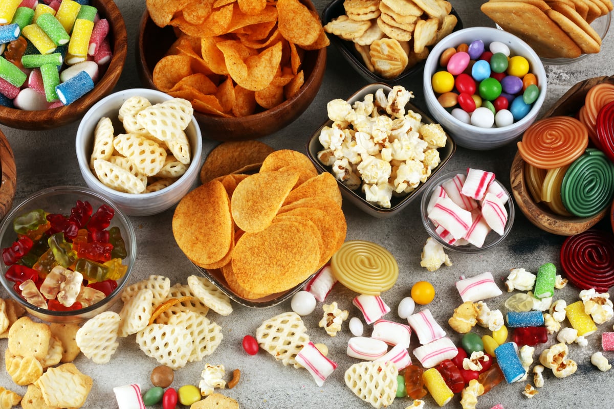 Multiple bowls full of a variety of snacks, including colorful candies, barbecue potato chips, crackers and popcorn.