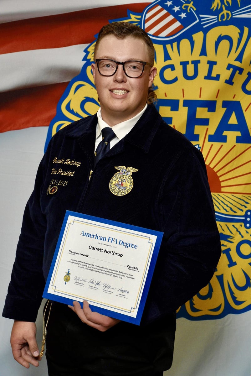Garrett stands in front of an FFA banner holding their FFA degree.