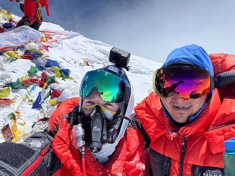 Two males in winter gear at the summit of Mount Everest