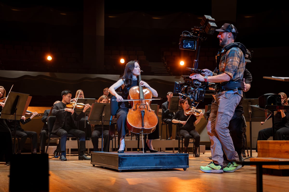 Behind the scenes of 'Never Dream Alone' at the Colorado Symphony. The symphony plays on stage while a camera operator stands to record the music.