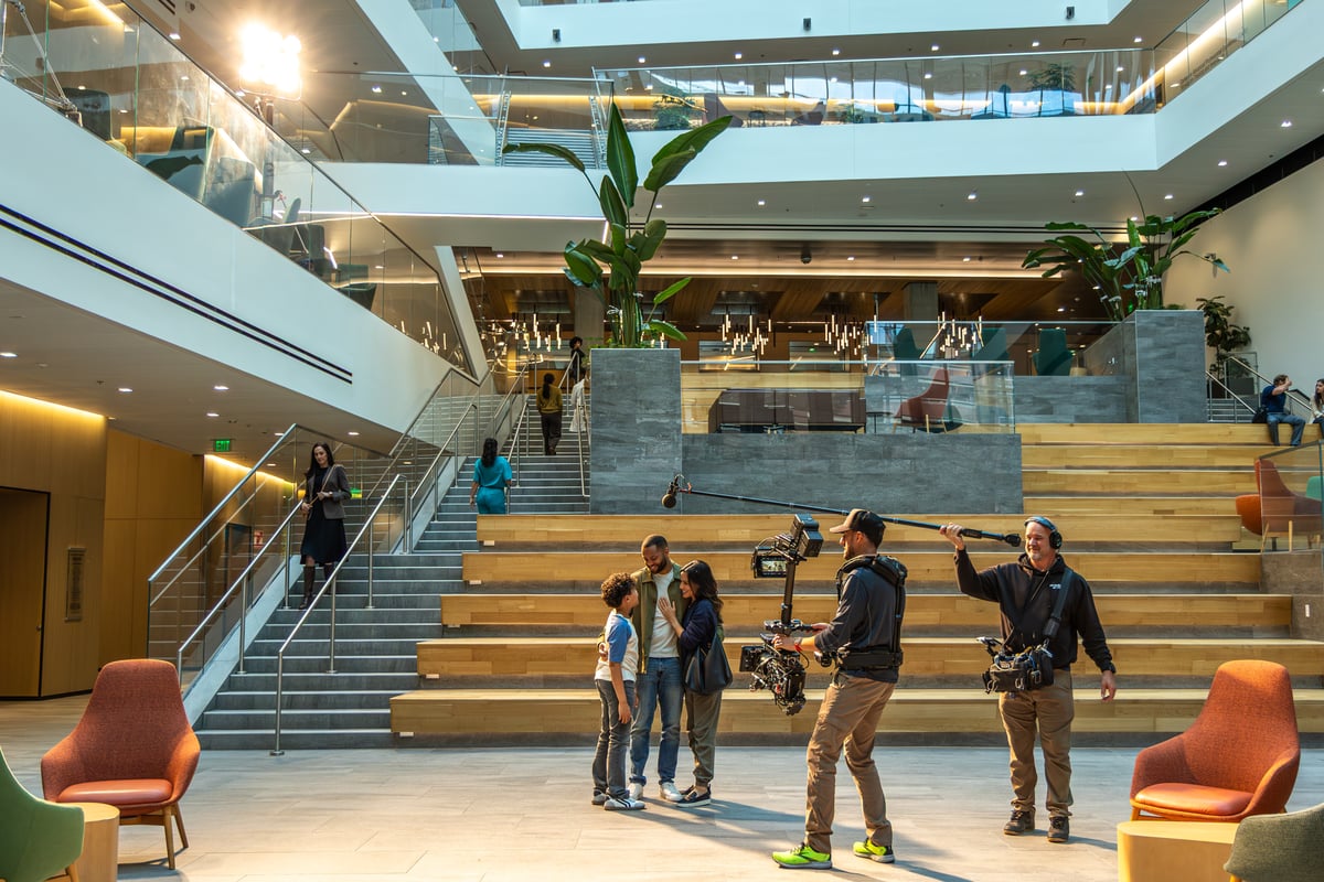 Behind the scenes footage of a camera operator and mic operator filming a group of three people at the CU Anschutz Health Sciences Building atrium.