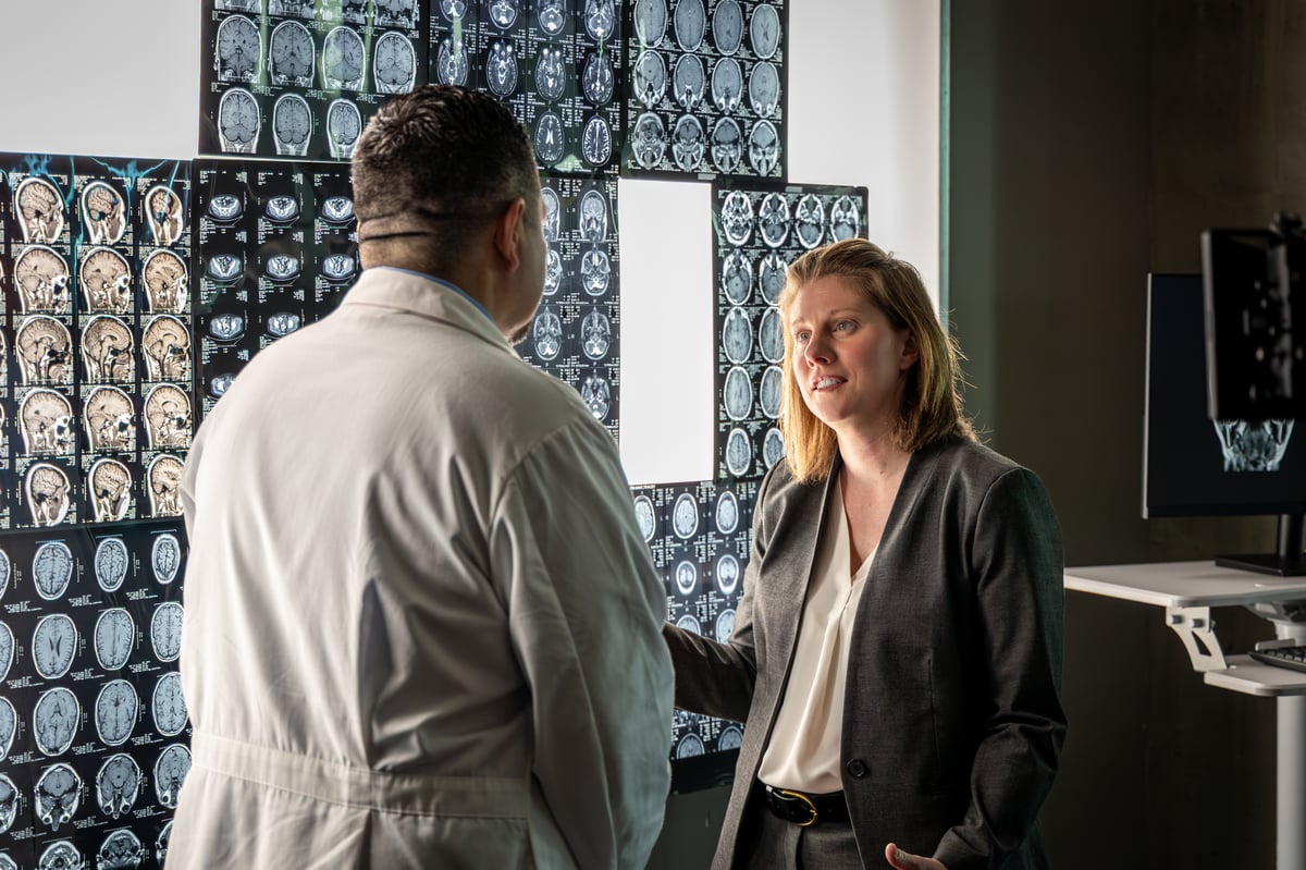 Amanda Piquet stands with a colleague in front of a series of brain scans during 'Never Dream Alone' filming.